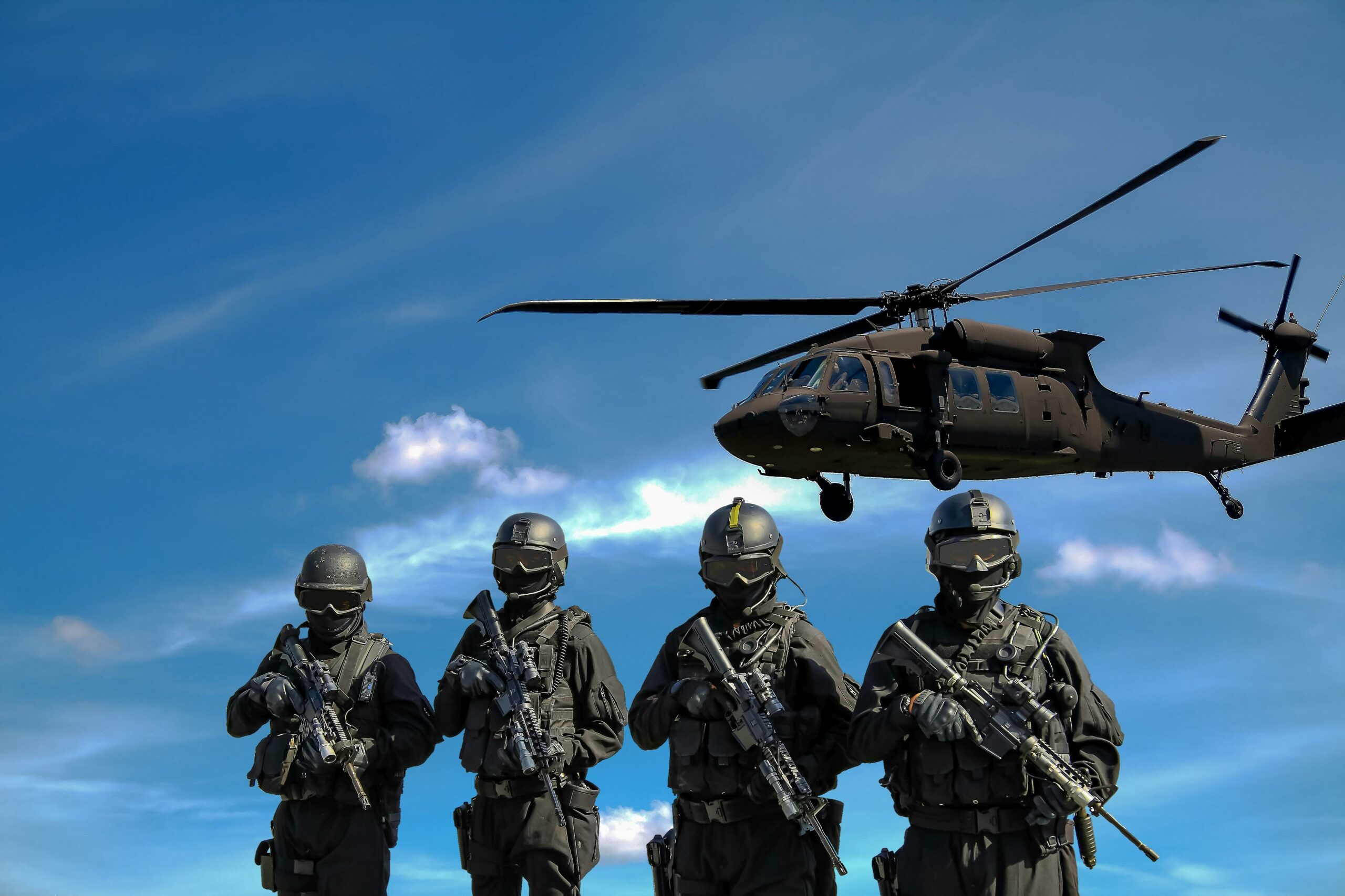 Four soldiers with a helicopter hovering behind them.